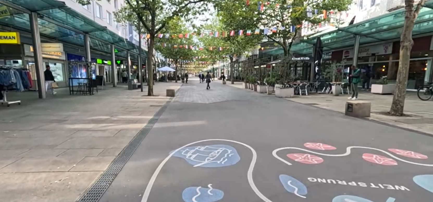 Bürgerstraße mit Glasarkaden, Bäumen und bemaltem Pflaster